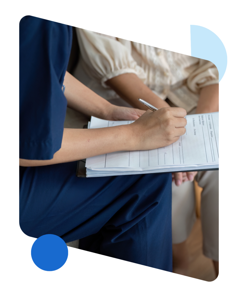 Close up of a person's hands holding a pen as they help someone complete a paper application on a clipboard. 