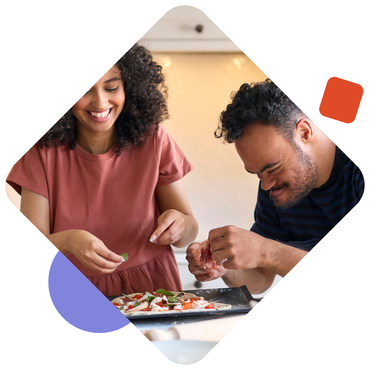 Man with Down Syndrome at home with his partner putting toppings on a pizza in the kitchen together. 