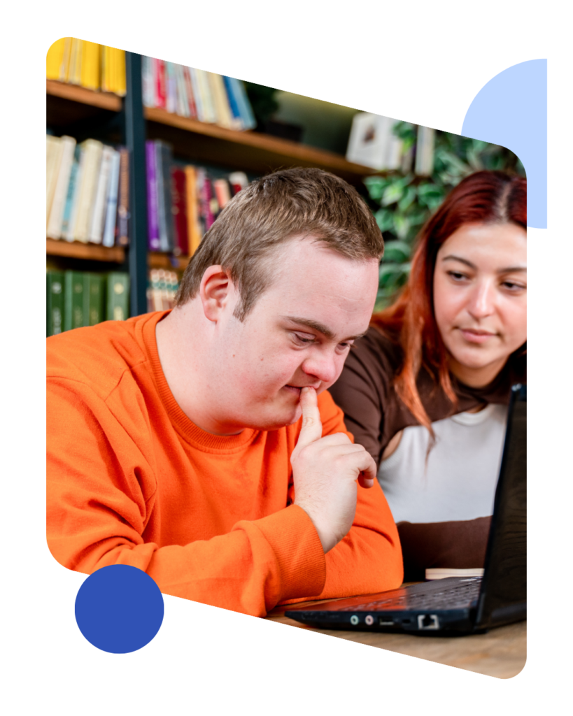 Young man with Down syndrome and his tutor studying on a laptop in a library.
