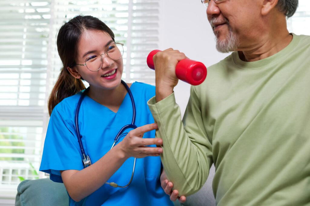 Young physical therapist helping an elderly Asian man do physical therapy by lifting weights at home.
