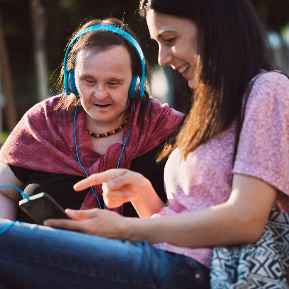 Middle-aged woman with Down Syndrome and her friend having fun and listening music in a park.