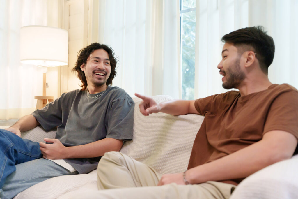 Two Asian friends having a cheerful conversation while relaxing on a sofa in a cozy living room.