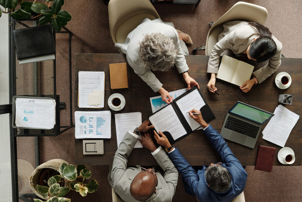 Overhead view of a group of middle aged multiethnic people collaborating around a table, reviewing documents and using laptop.