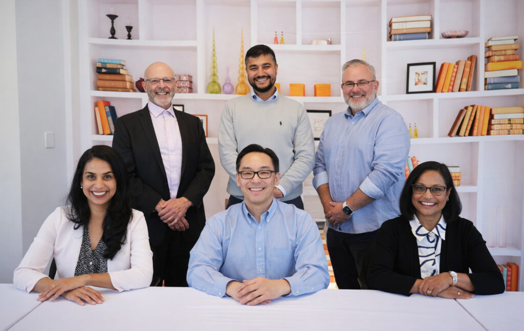 Six of GGRC's leadership team members sitting at a table, smiling at camera. There's a white bookshelf filled with books behind them. 