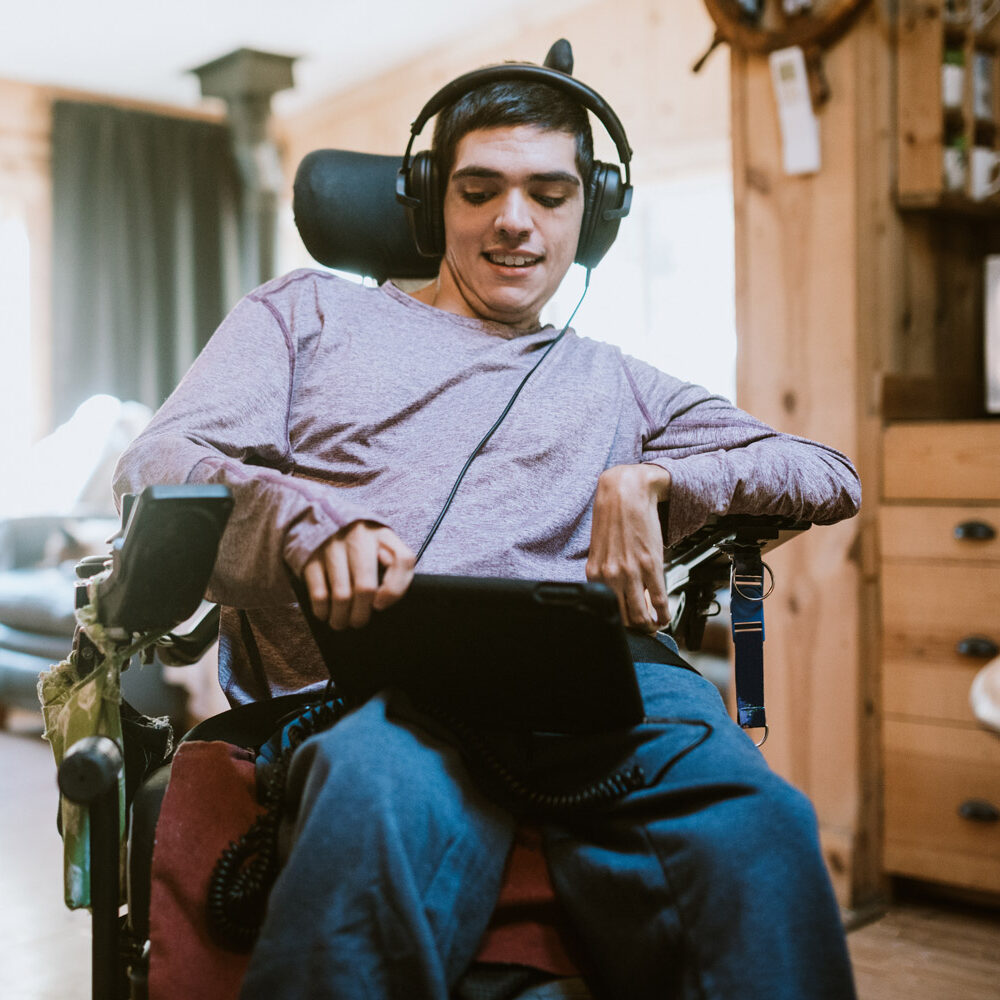 Confident young man in a wheelchair at home using an iPad and listening to a video with headphones on.