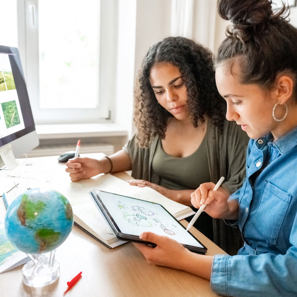 Two young women in a home office preparing documents together on an iPad.