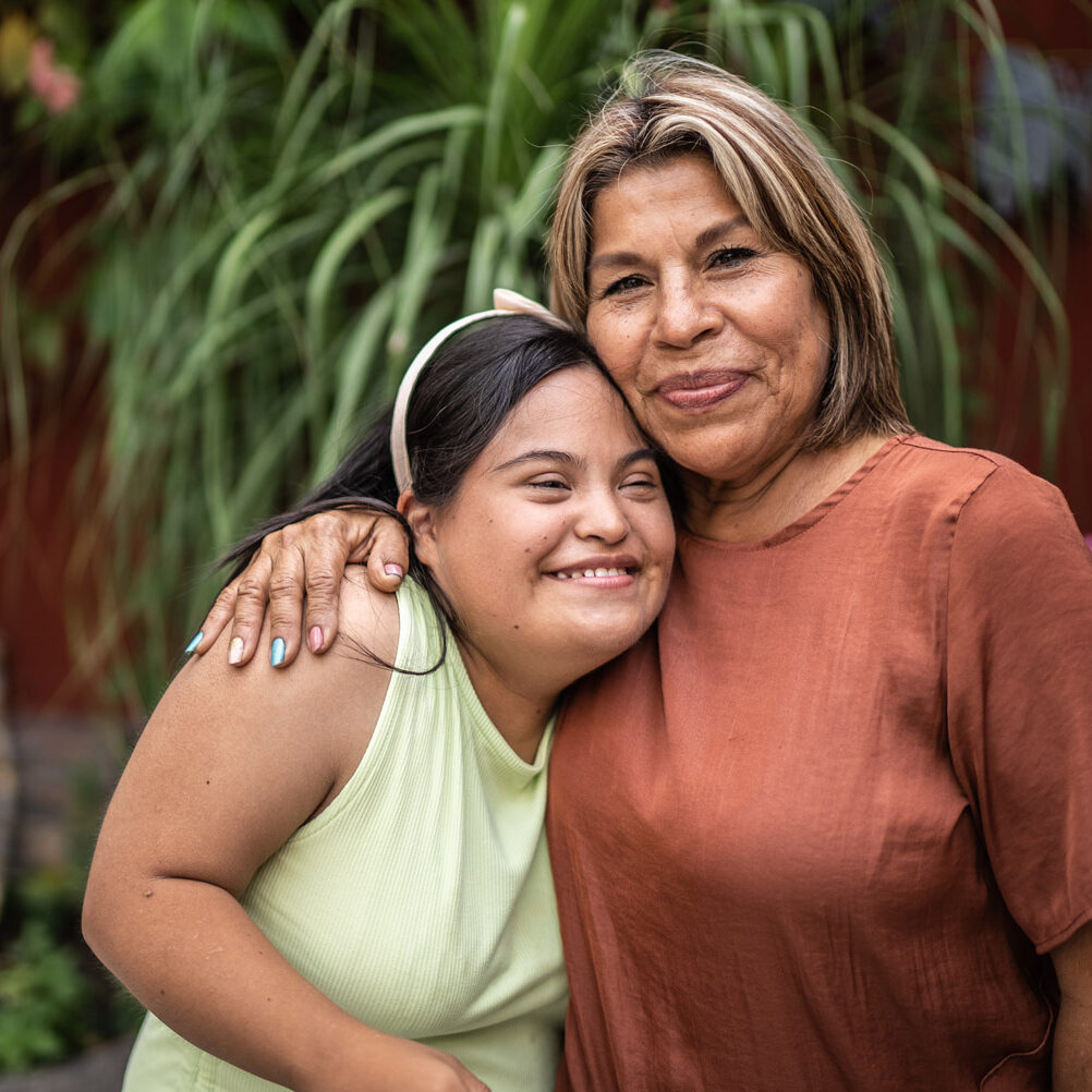 Outdoor portrait of mother embracing her daughter with Down Syndrome.