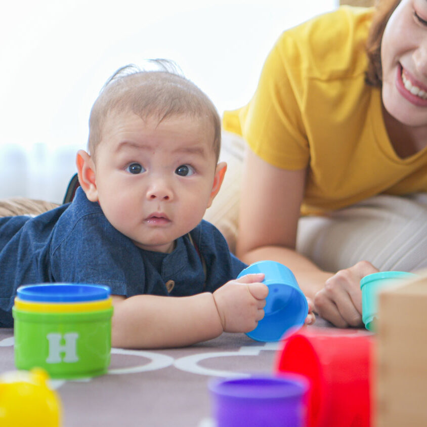 A tiny child cheerfully plays with toys on the floor of the living room with an adult woman.