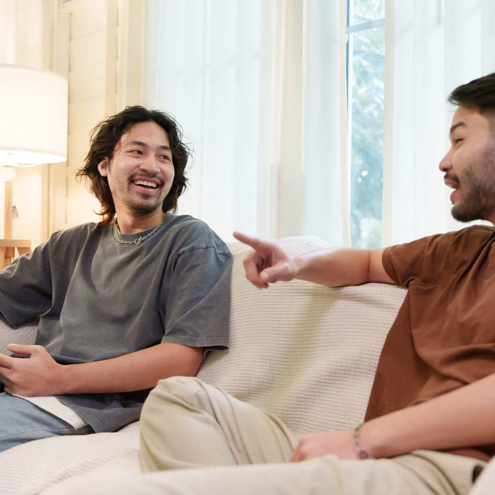 Two Asian friends having a cheerful conversation while relaxing on a sofa in a cozy living room.